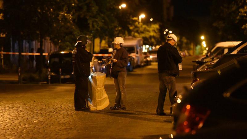 Ermittler mit Schutzhelmen sichern die Spuren nach dem Angriff auf den Funkwagen, der mit Steinen beworfen wurde (Foto: spreepicture)