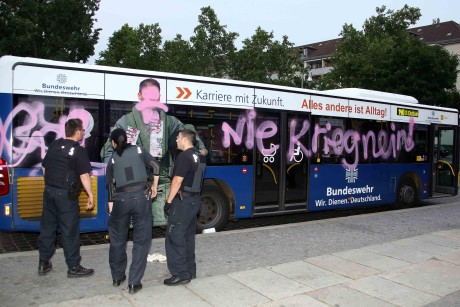 Beschädigt: Drei Polizeibeamte inspizieren den BVG-Bus, auf den maskierte Unbekannte Parolen wie "Nie Krieg Nein" gesprüht haben