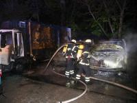 Zwei Einsatzkräfte löschen die Reste der Kühlwagen. In der Nacht zu Freitag wurden diese mutmaßlich von Feuerteufeln in Brand gesteckt.