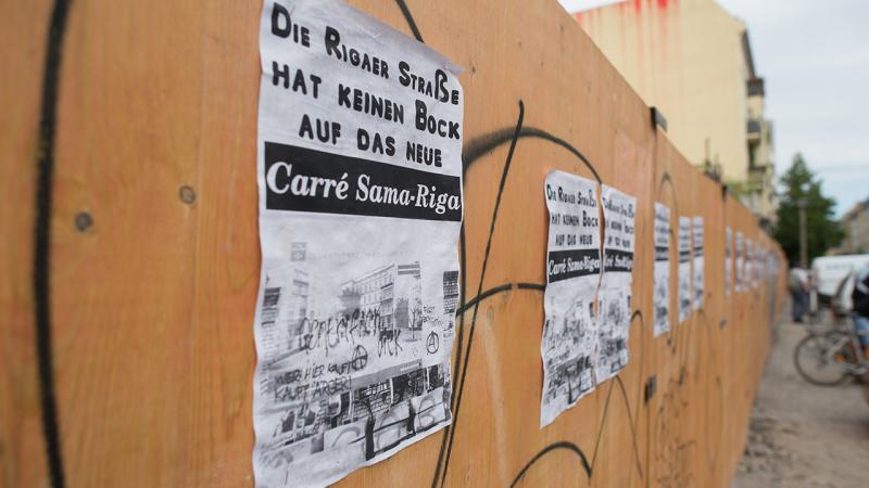 "Die Rigaer Straße hat keinen Bock auf das neue Carre Sama-Riga" steht auf Zetteln, die am 16.07.2016 in Berlin in der Rigaer Straße an einem Bauzaun kleben